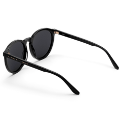 Arch Bio-Acetate Black sunglasses with round black frames, dark lenses, and gold Daniel Wellington branding along the arm.