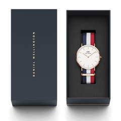 Classic Cambridge Rose Gold watch with a blue, white, and red NATO strap presented in an elegant Daniel Wellington gift box.