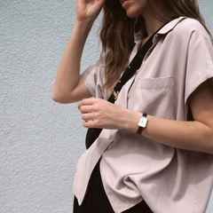 A woman wearing the Daniel Wellington Quadro Pressed Sheffield watch, featuring a rectangular eggshell white dial, rose gold case, and black leather strap, styled with a relaxed short-sleeve shirt and crossbody bag.