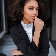 Woman wearing the Elan Unity Necklace Silver with two interlocking rings on a delicate chain, styled with a matching bracelet and a black blazer over a white turtleneck.