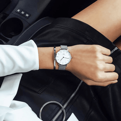 Petite Sterling silver mesh women’s watch with white dial, styled with a bangle and black leather skirt in a car setting.