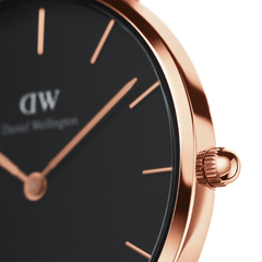 Detail of Daniel Wellington Petite Melrose watch with black dial, rose gold case, and minimalist hour markers and crown.
