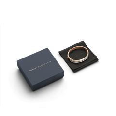 Emalie Infinite Rose Gold Satin White bracelet displayed on a black leather pouch next to a navy Daniel Wellington gift box.