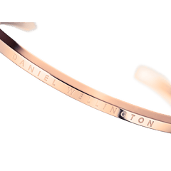 Polished rose gold Daniel Wellington Classic Bracelet with engraved logo, minimalist open cuff design, close-up detail.