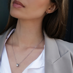 A woman wearing the Elan Necklace Silver, featuring a polished silver ring pendant on a fine adjustable chain, styled with a white blouse and beige blazer.