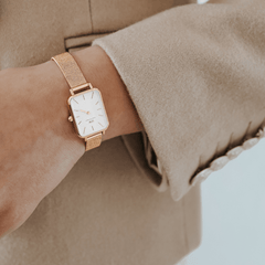 Quadro Pressed Melrose watch with a rectangular eggshell white dial and rose gold mesh strap, styled on a wrist with a beige coat.