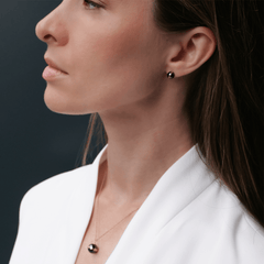 Woman wearing Aspiration Earrings in rose gold and black ceramic, styled with a matching necklace and a white blazer for an elegant, modern look.