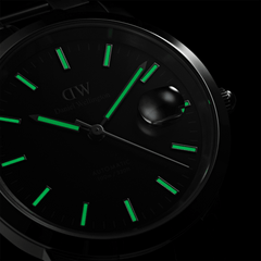 Close-up of the Iconic Link Automatic watch dial in the dark, highlighting luminous hands and hour markers with a magnified date window.